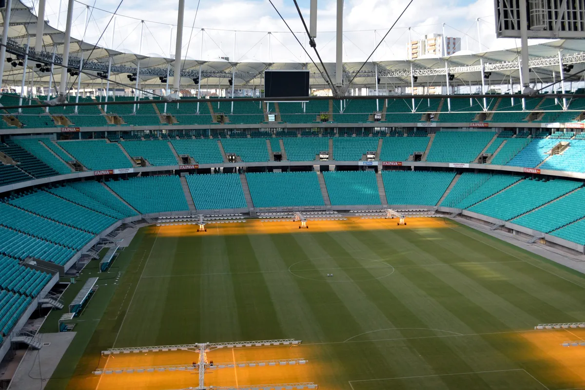Inside the Arena Fonte Nova in Salvador, with the green pitch, the center circle and three tiers of teal seats under a white roof