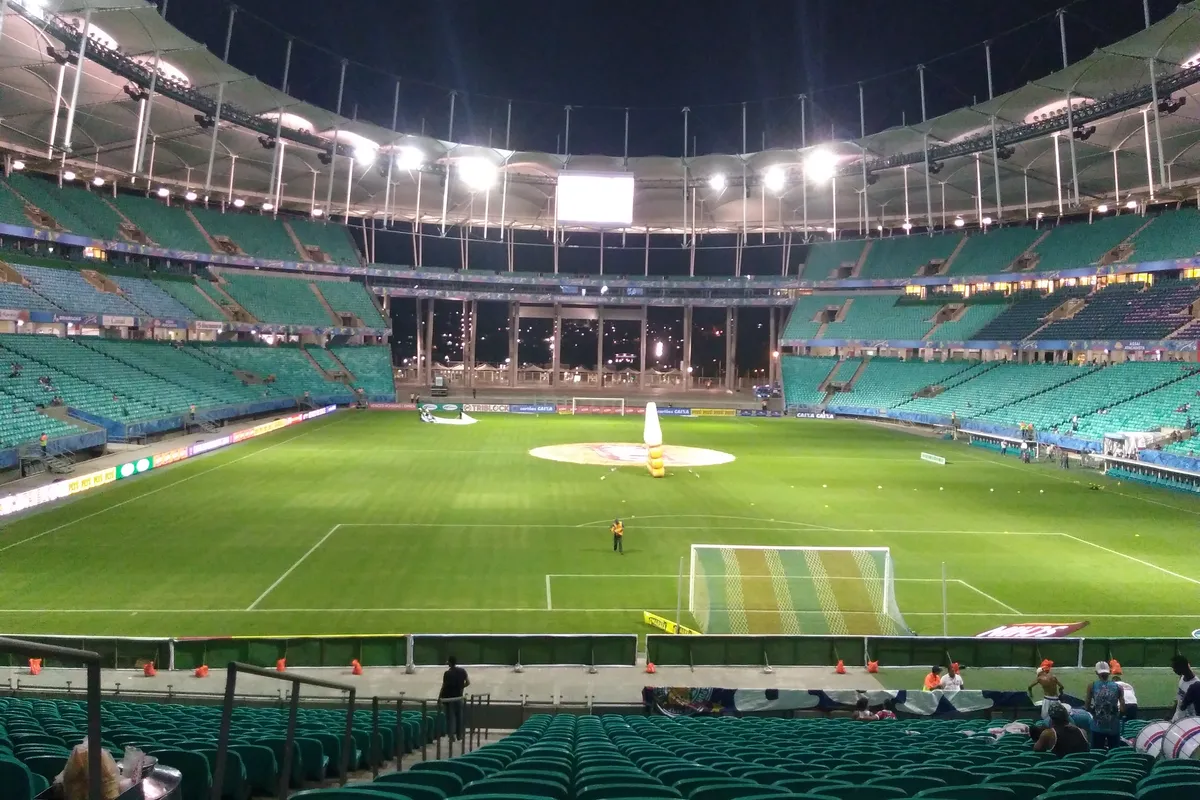Inside the Arena Fonte Nova at night, with floodlights along the white roof, the lit green pitch and teal seats in the stands
