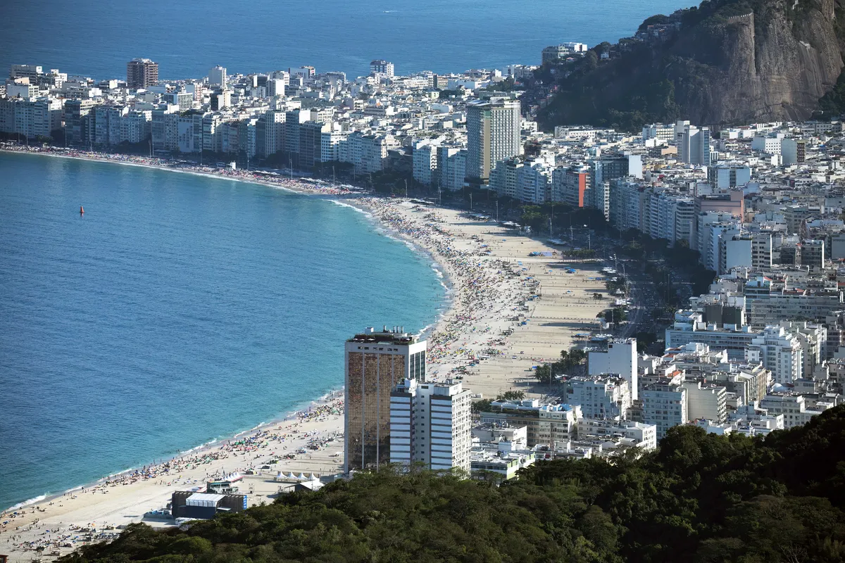 View from above of Copacabana beach in Rio de Janeiro, with the curved shoreline, apartment buildings along the avenue and a green hill in the foreground