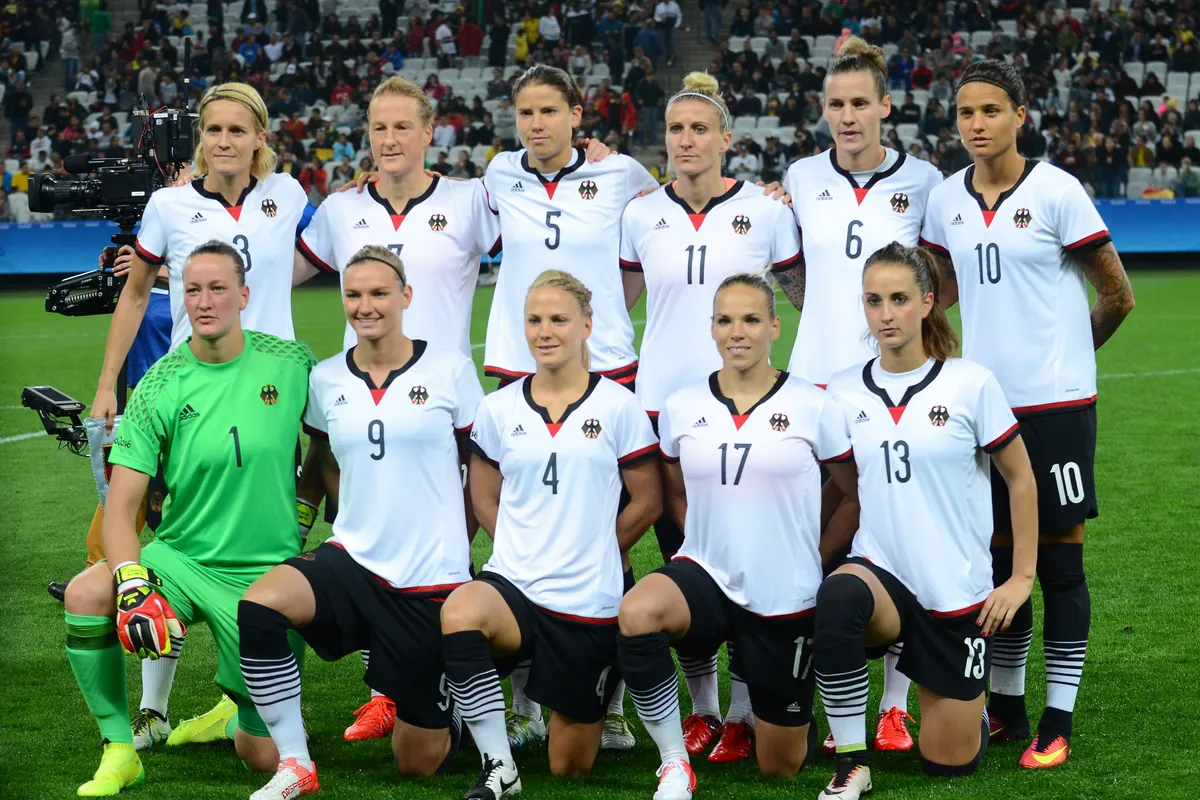 Germany's women's national team players in white shirts line up in two rows on the pitch, some kneeling, before a match at a stadium in São Paulo