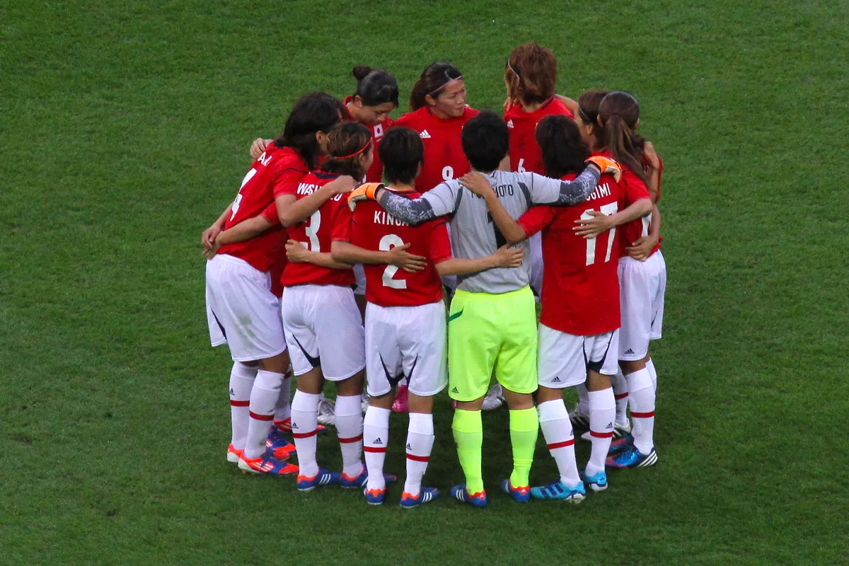 Japan's players in red shirts and white shorts stand in a tight huddle on the grass before a match