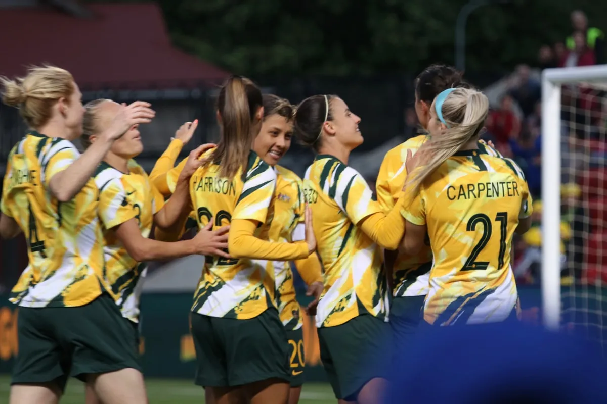 Australia's Matildas players in gold and green jerseys hug each other while celebrating a goal