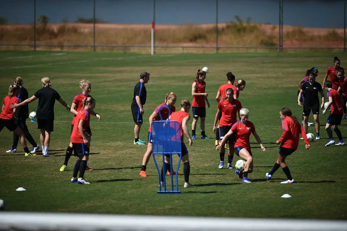 U.S. women's national team players in red shirts run passing drills on a training field in Brasília with orange and blue cones