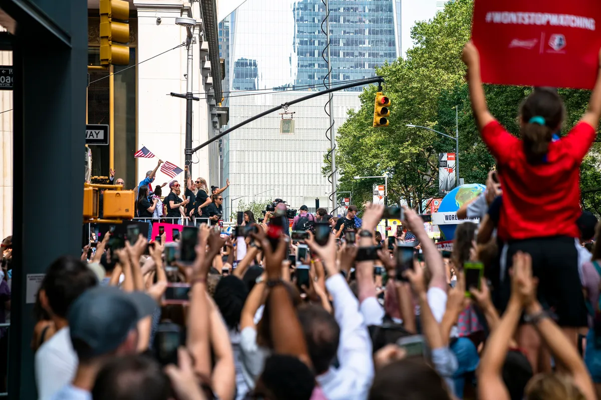 Crowd in New York holding up phones and signs to film the U.S. women's team on a float during the 2019 World Cup champions parade
